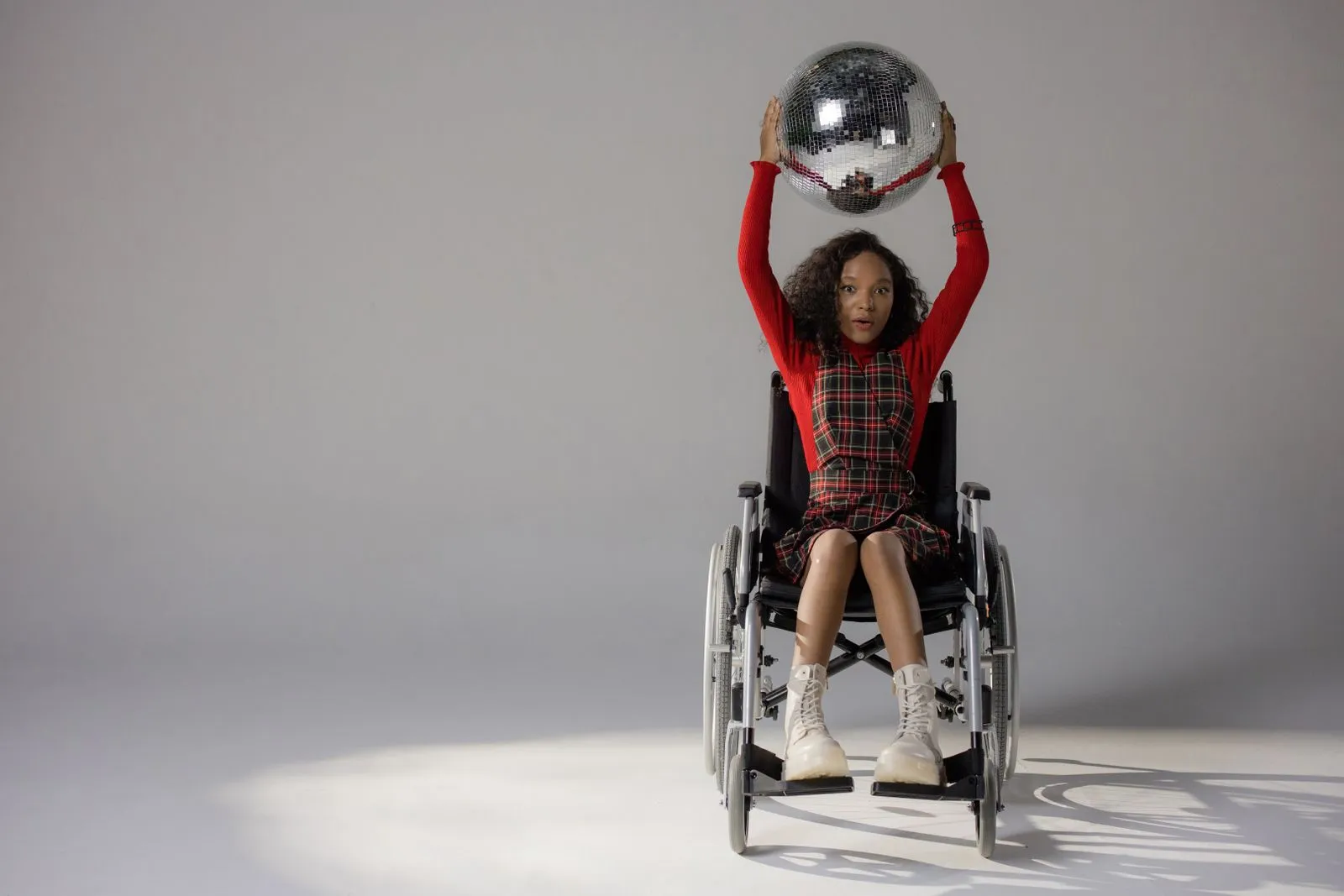 Stylish young woman in a wheelchair holding a disco ball in a studio setting.